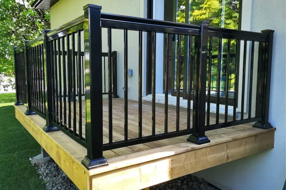 Timber deck with black aluminum picket railings and a matching gate beside a home