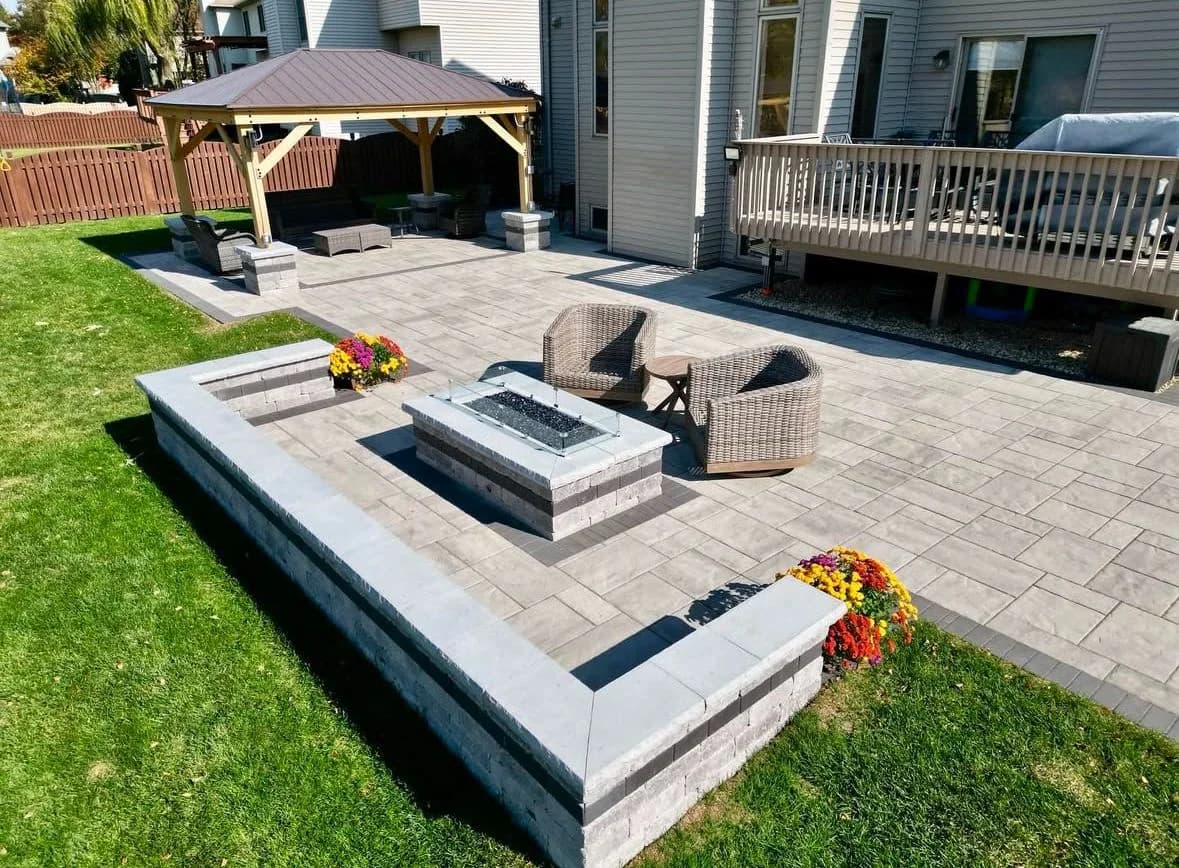 Large grey interlocking patio with seating walls, an adjoining raised deck and timber fencing