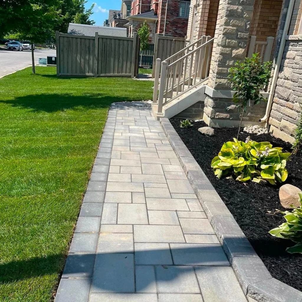 Interlocking walkway beside a brick home with a lawn and flower border